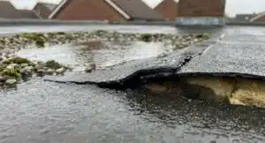 Plat dak met water dat zich ophoopt en beschadigde bitumennaad die scheurt en loslaat.