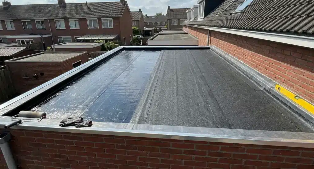 Plat dak met twee verschillende bitumen membranen naast elkaar: links een donkerblauwe APP-laag en rechts een grijze