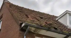 Pannendak met zichtbare schade: losliggende tegels, mossen en algengroei, en verkleurde pannen die vervangingsbehoefte