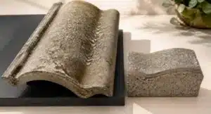 Verweerde betonnen dakpan met grijze patina en structuurdetails, intact maar met zichtbare ouderdom en afzetting.